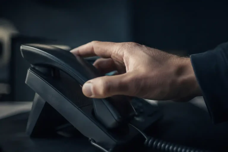 Sécuriser sa téléphonie IP : une main repose le combiné d’un téléphone IP de bureau, dans un bureau sombre